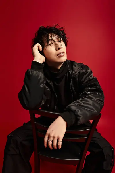 Stylish young man rests on a chair against a red backdrop, radiating confidence and modern elegance. — Stock Photo