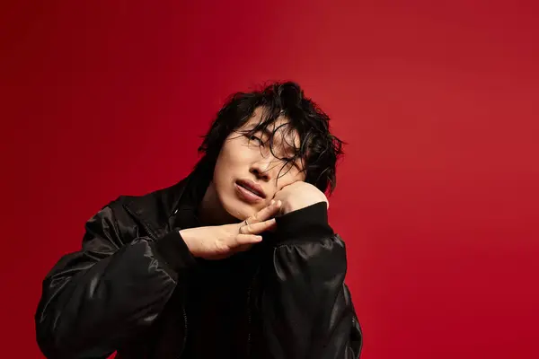 Stylish Asian man rests head on hands in a red studio. — Stock Photo