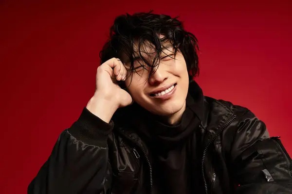 A young asian man strikes a fashionable pose in a red studio setting. — Stock Photo
