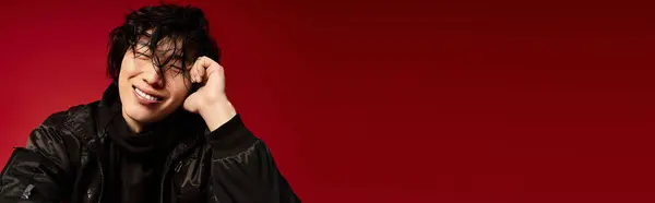 Young Asian model in black jacket smiles warmly in red-lit studio, banner — Stock Photo