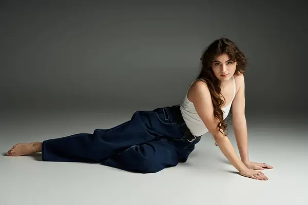 A young woman shows off her stylish denim in a minimalist studio, exuding confidence. — Stock Photo