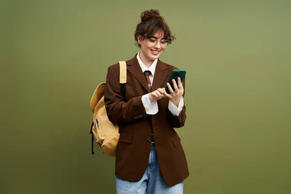 A stylish young woman in a brown blazer and jeans smiles while texting. — Stock Photo