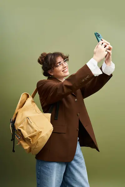 A cheerful young woman smiles in a selfie, showing off her trendy outfit and backpack. — Stock Photo