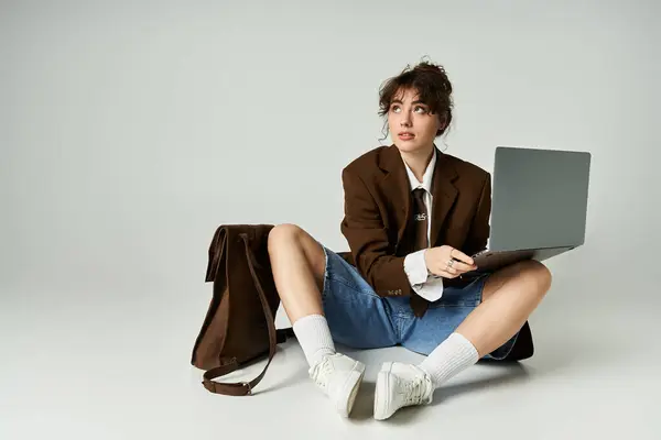 Giovane donna in abiti eleganti si siede sul pavimento, focalizzata sul suo computer portatile. — Foto stock