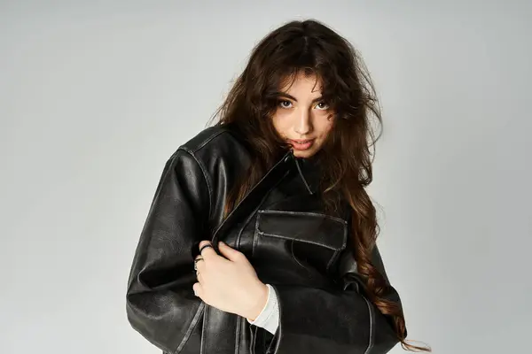 A young woman with long hair poses confidently in a sleek black jacket, showcasing her style. — Stock Photo