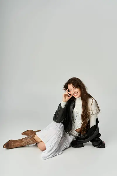 Charming young woman in stylish outfit poses confidently while seated on a smooth surface. — Stock Photo