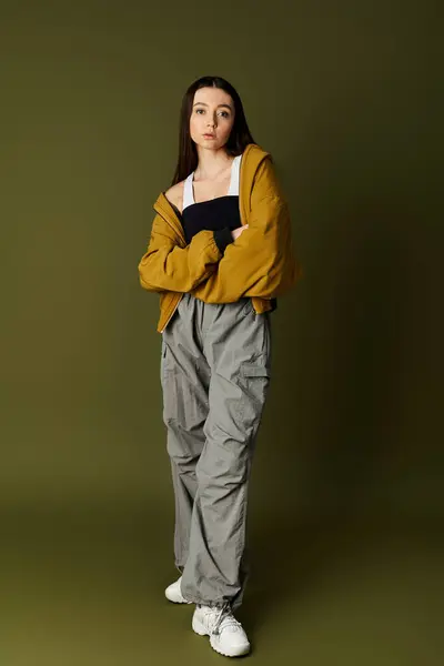 Une jeune jolie femme dans une tenue chic se dresse en toute confiance sur un fond discret, style rayonnant. — Photo de stock
