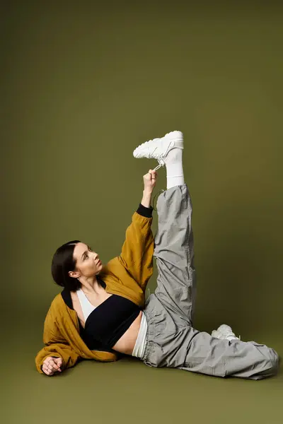 A young woman elegantly poses with one leg raised, showing off her stylish outfit indoors. — Stock Photo