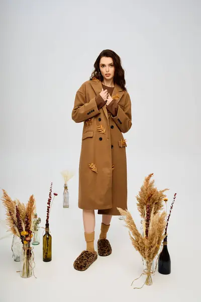 A beautiful young woman stands gracefully in a coat, surrounded by flowers in springtime. — Stock Photo