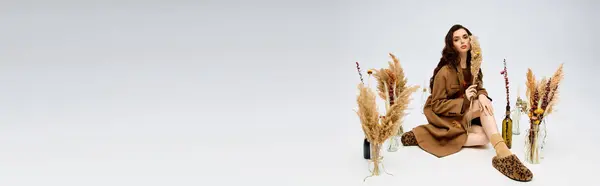 A young woman with long brown hair sits gracefully among spring flowers and feathers, banner — Stock Photo