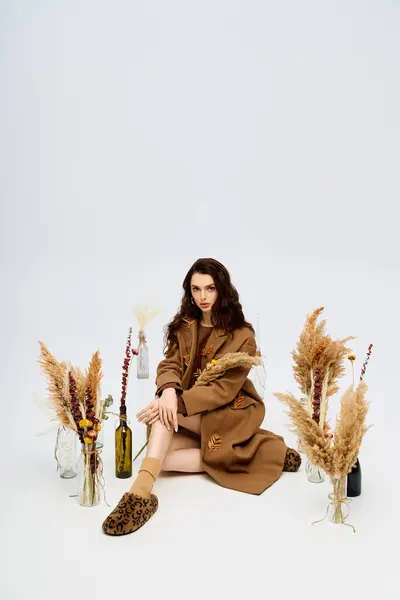 A beautiful young woman with long hair wears a coat while sitting among flowers. — Stock Photo