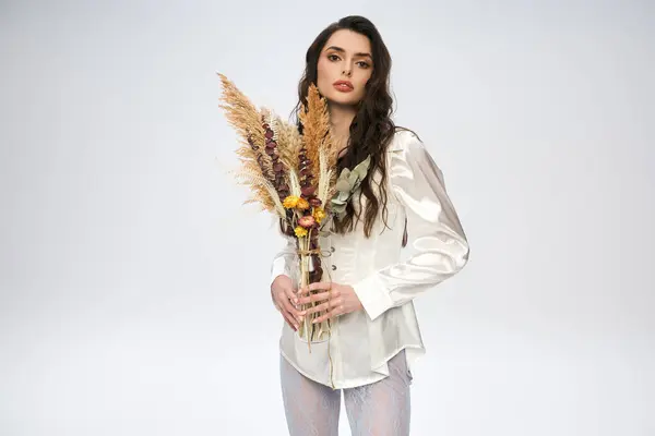 Beautiful young woman with brown hair is amidst colorful flowers in a serene studio environment. — Stock Photo