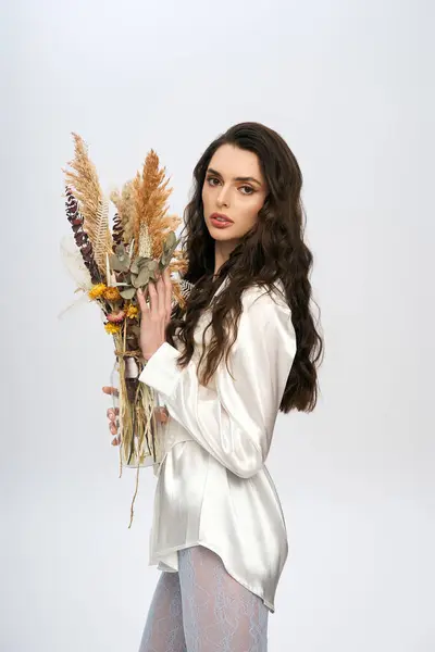 A young woman with brown hair holds a bouquet of flowers, radiating spring joy in a studio setting. — Stock Photo