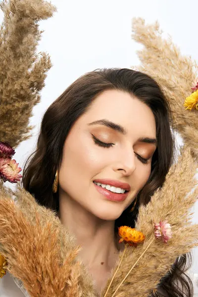 A young woman with brown hair smiles gently, surrounded by colorful flowers and soft plants. — Stock Photo