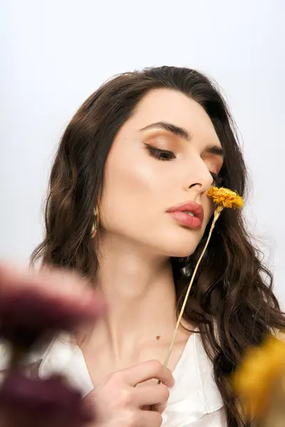 A beautiful young woman with brown hair gently holds a flower, embracing the joy of springtime. — Stock Photo