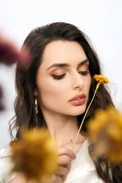 Une jeune femme tient doucement une fleur, perdue dans la pensée au milieu de fleurs colorées au printemps. — Photo de stock