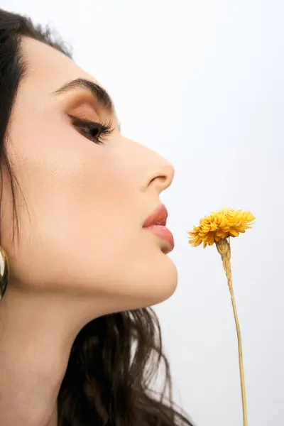 A beautiful young woman with brown hair is captivated by vibrant flower during spring in a studio. — Stock Photo