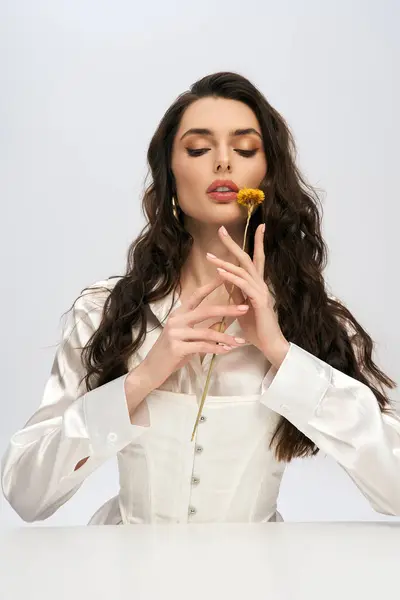 A beautiful young woman with brown hair gently holds a flower, surrounded by spring elegance. — Stock Photo