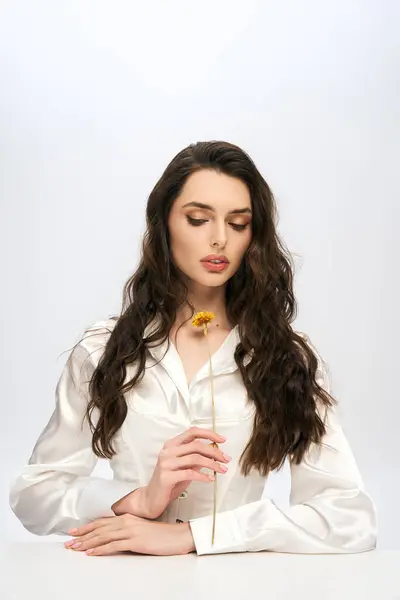A young woman with flowing brown hair delicately holds a flower, embodying spring beauty. — Stock Photo
