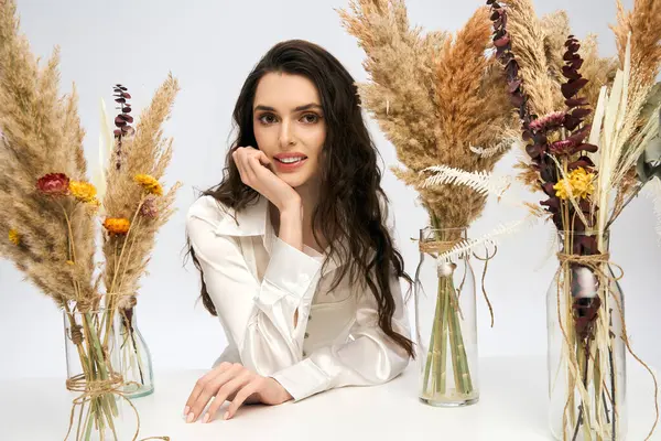 A beautiful young woman with brown hair is surrounded by colorful spring flowers in a studio. — Stock Photo
