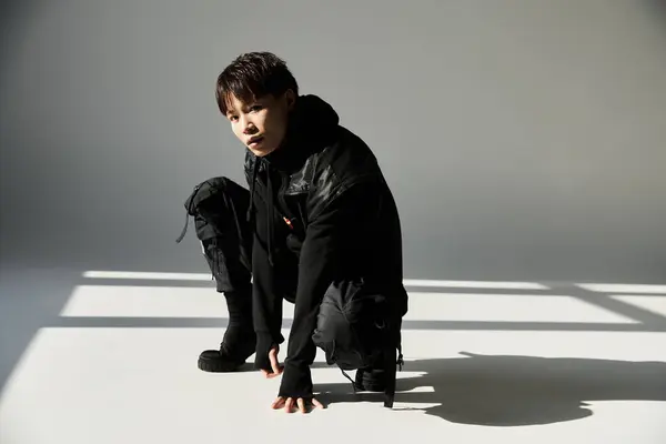 A stylish Asian man kneels on a clean surface, showcasing his trendy outfit in soft shadows. — Stock Photo