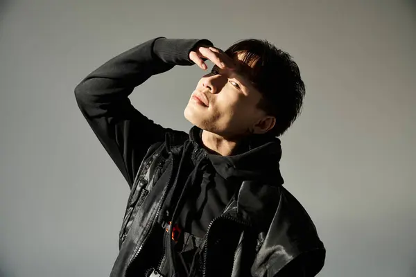 Handsome young man stands confidently, shielding his eyes from light, showcasing a stylish outfit. — Stock Photo