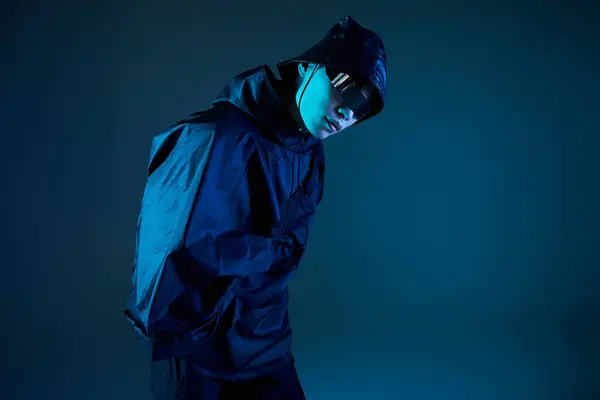Youthful asian man showcases modern street style with confidence in vibrant blue lighting indoors. — Stock Photo
