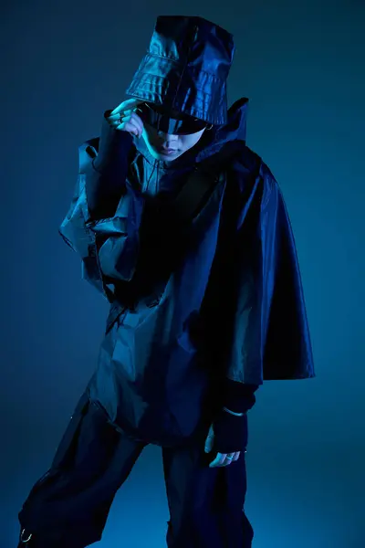 A stylish young Asian man poses in a dark outfit amid a blue toned studio backdrop. — Stock Photo