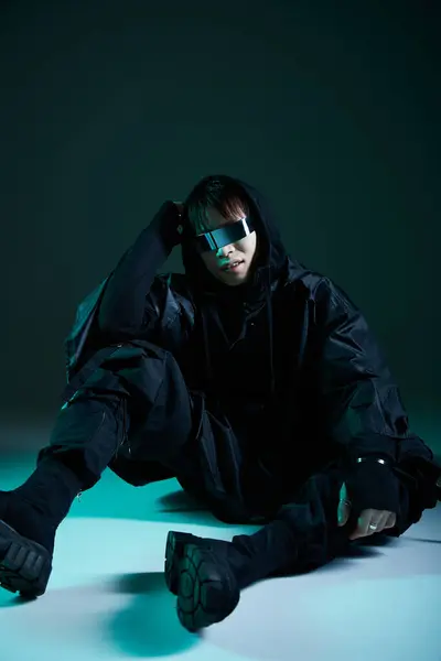 Handsome young Asian man dressed in a sharp black outfit strikes a fashionable pose in low light. — Stock Photo