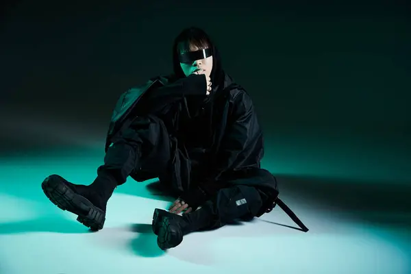 Handsome young man dressed in black streetwear, sitting on the ground in a stylish pose. — Stock Photo
