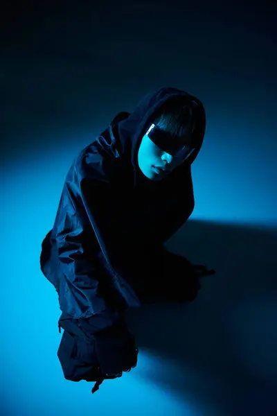 A handsome young man dressed in black is striking a captivating pose against a moody blue backdrop. — Stock Photo