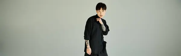 A stylish young man stands confidently in a studio, tattoos visible on his outfit. — Stock Photo