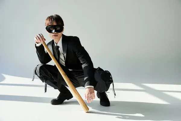 A young, dapper man wearing a mask crouches stylishly with a bat, showcasing a confident demeanor. — Stock Photo