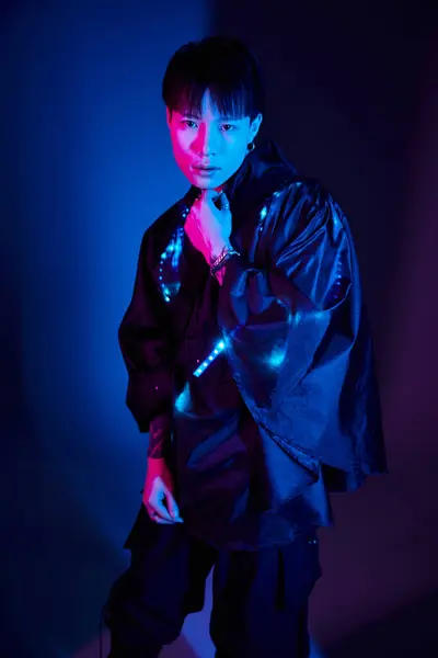 Bel homme asiatique pose avec confiance dans une tenue unique dans un frappant bleu et violet toile de fond. — Photo de stock