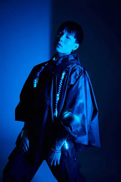 Ein hübscher junger asiatischer Mann strahlt in einem stilvollen Outfit in einer blau beleuchteten Umgebung Zuversicht aus. — Stockfoto