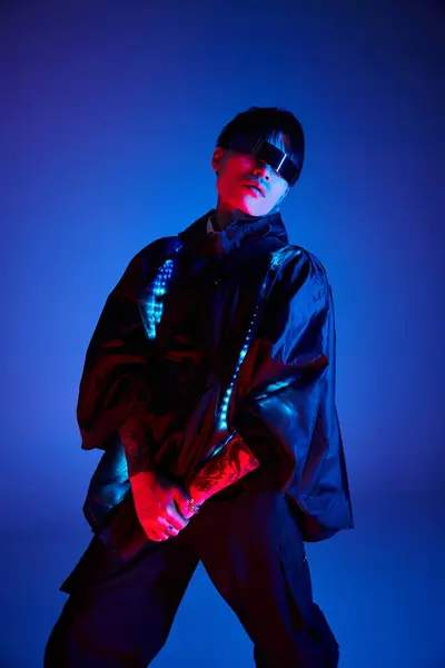 Handsome young man showcases his stylish attire and confident pose under striking blue lighting — Stock Photo
