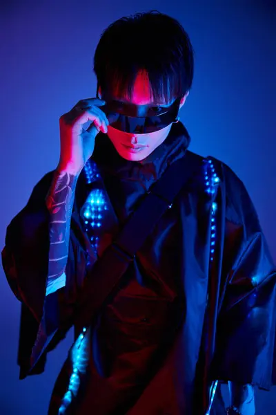 Ein modischer junger Mann posiert selbstbewusst mit schnittiger Sonnenbrille unter grellem Neonlicht. — Stockfoto