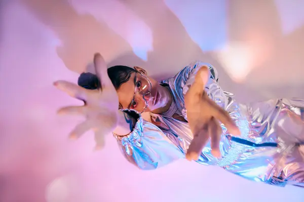 A young woman showcases holographic fashion in an experimental pose among vibrant colors. — Stock Photo