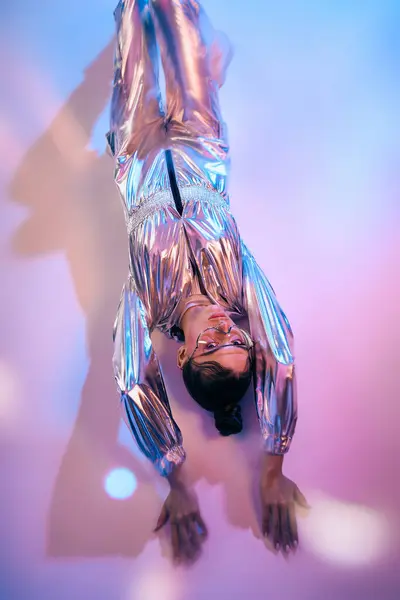 Woman dressed in shiny holographic clothing interacts with surreal colors in a contemporary space. — Stock Photo