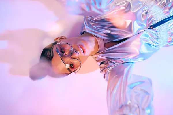 A young woman poses in a sleek metallic outfit, highlighting her beauty in holographic hues. — Stock Photo