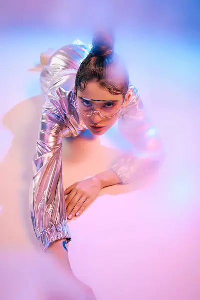 A young woman in metallic fashion lies gracefully while surrounded by holographic colors and mist. — Stock Photo