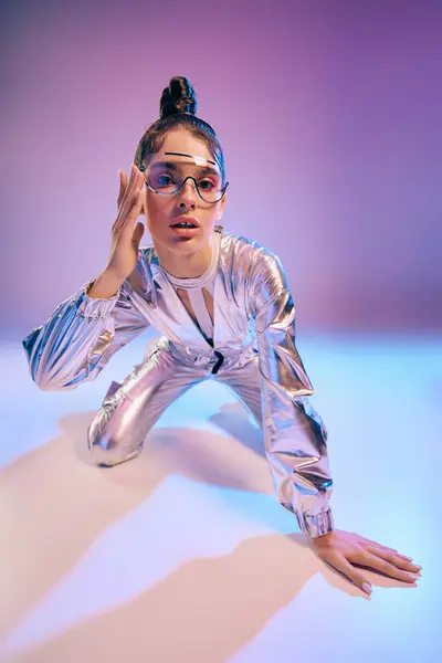 A young woman kneels in a shiny metallic outfit, showcasing futuristic fashion with artistic flair. — Stock Photo