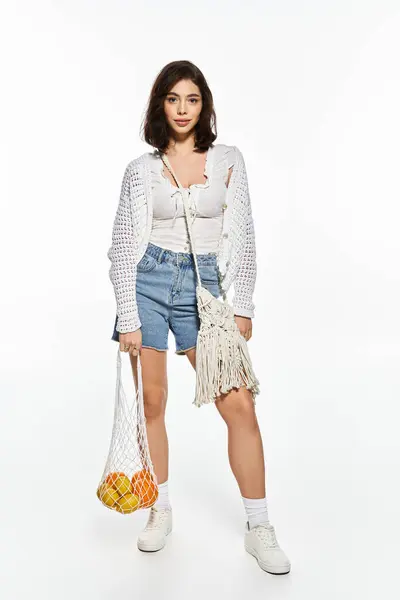 Stylish young woman showcases her trendy summer look while holding a net bag of oranges. — Stock Photo