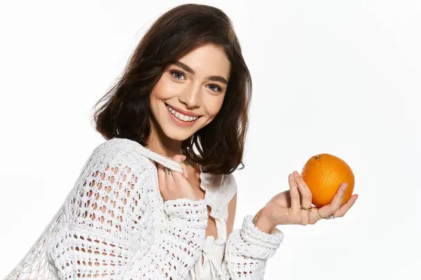 A brightly dressed woman smiles with a fresh orange, radiating joy in a minimalist space. — Stock Photo