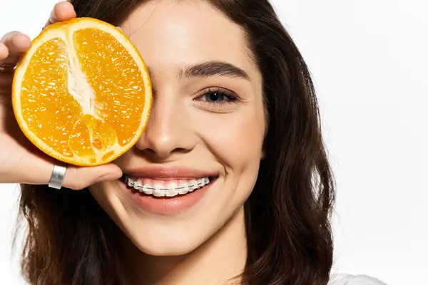 Young woman in trendy summer attire playfully holds an orange near her smile, exuding joy. — Stock Photo
