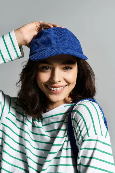 Une jeune femme porte un haut rayé à la mode et une casquette bleue, rayonnant de joie et de style d'été. — Photo de stock