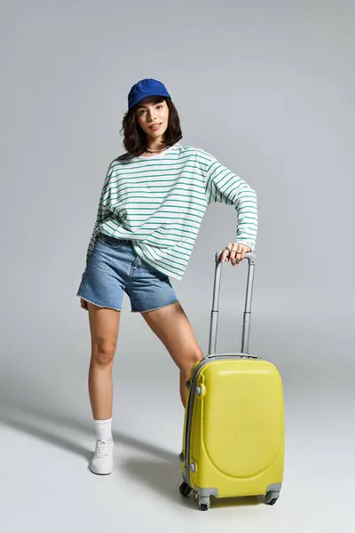 Jeune femme en tenue tendance pose en toute confiance avec sa valise jaune, embrassant les vibrations de l'été. — Photo de stock