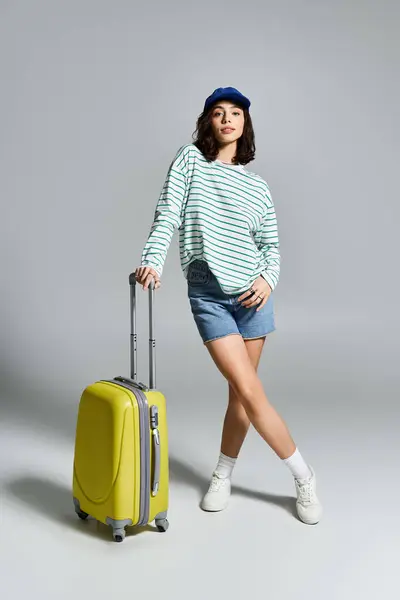 Jeune femme en tenue d'été élégante pose en toute confiance avec une valise lumineuse, excitée pour les voyages. — Photo de stock