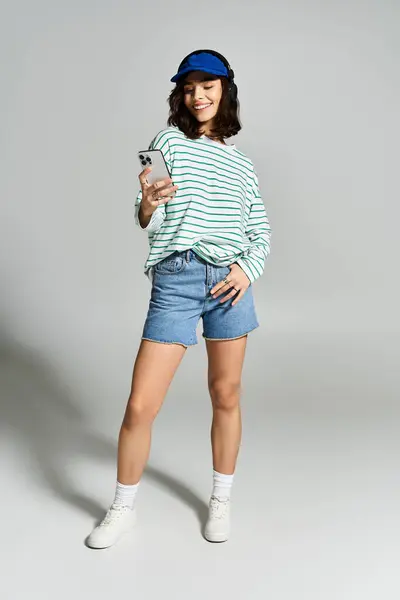 Joyful woman in stylish summer outfit engages with her smartphone, showcasing casual fashion. — Stock Photo