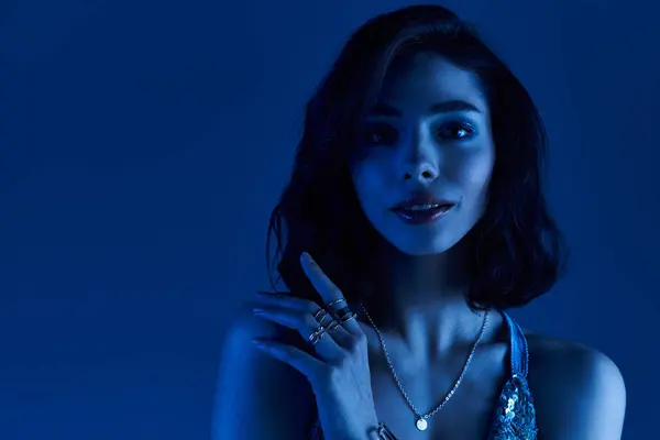 A confident young woman models stylish summer wear under striking blue light, radiating charm. — Stock Photo